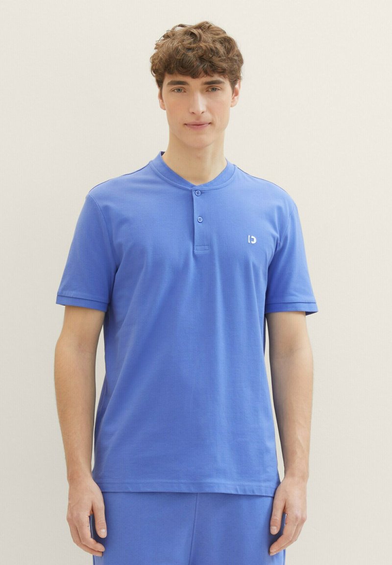 Modrá polokošile s krátkým rukávem a zapínacím límcem, vyrobená z měkké bavlny. Na levé straně se nachází malé logo.
