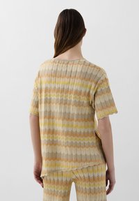 Knit top with short sleeves featuring a wave pattern in beige, orange, yellow, and gray. Scalloped edges and ribbed texture.