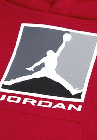 Tessuto rosso con una superficie liscia decorato con il logo Jumpman in nero e grigio. Il logo rappresenta una figura che salta per schiacciare un pallone da basket.