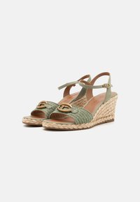 Zelené tkané espadrilky na klínku s nastavitelným páskem kolem kotníku a zlatou sponou na přední straně. Pletený jatečný střední podpatek.
