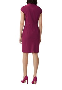 Figurbetontes, knielanges Kleid in dunklem Magenta mit kurzen Ärmeln, einem Reißverschluss im Rücken und einem hohen Ausschnitt. Getragen mit passenden rosa Stiletto-Absätzen.
