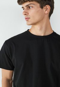 Czarny bawełniany t-shirt z klasycznym okrągłym dekoltem, krótkimi rękawami, gładką teksturą i dopasowanym krojem. Bez widocznych logo czy wzorów.