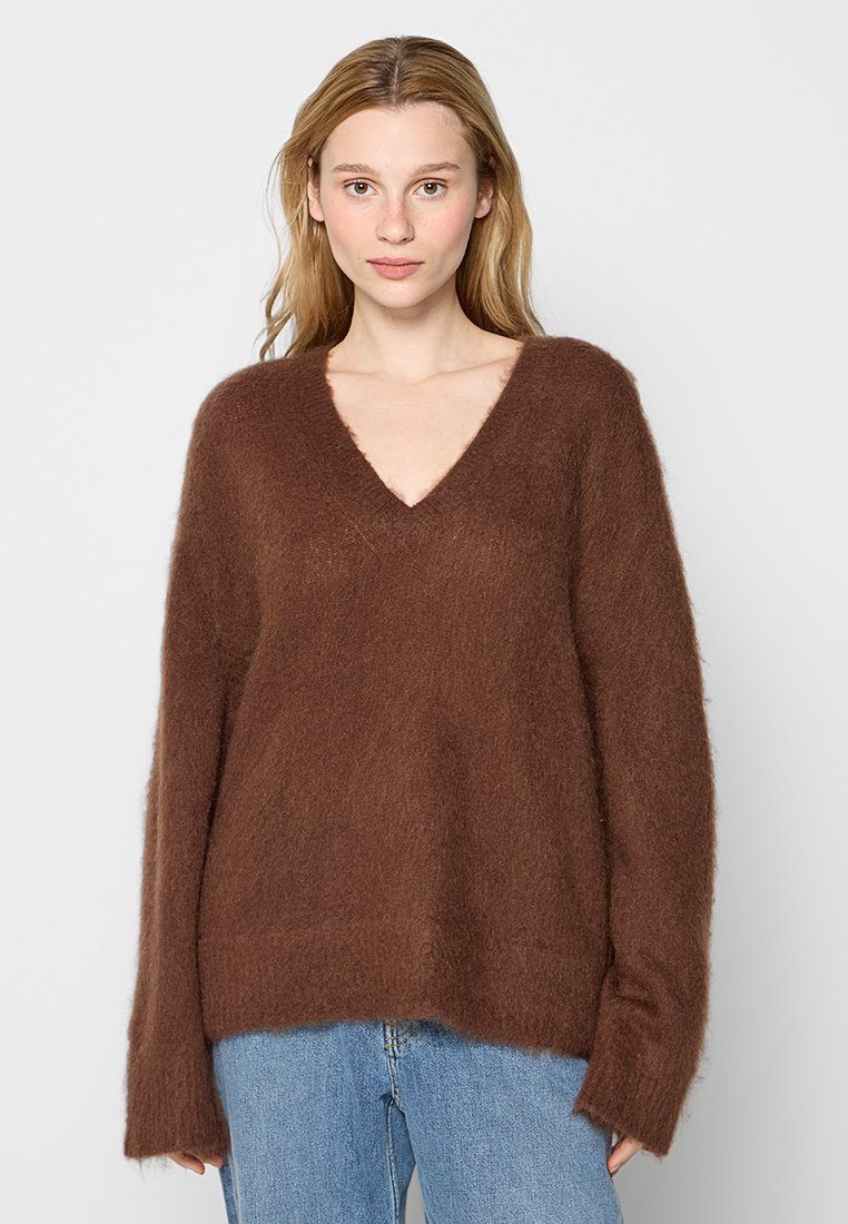 Pull en v beige, fluffy, avec des manches longues, coupe décontractée et texture douce, associé à un jean en denim bleu clair.