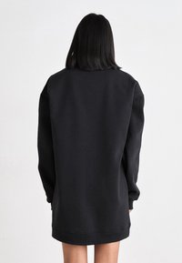 Svart oversized sweatshirt med långa ärmar, ribbade muddarna och rundad nederkant. Tillverkad av ett mjukt material, minimalistisk design, inga synliga mönster.