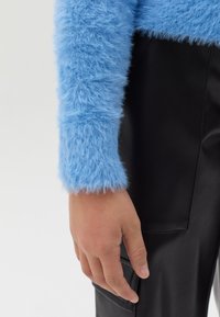 Blauwe pluizige trui met een gestructureerde afwerking, gecombineerd met zwarte leren broek met zijzakken.