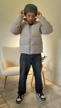 Svetlosivá prešívaná bunda s vysokým golierom, zapínaním na zips a bočnými vreckami. V kombinácii s tmavými džínsami a čierno-bielymi teniskami. Na hlave zelená čiapka.