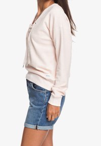Sweatshirt rose clair en rib avec un col en V et un détail à lacets, associé à un short en denim bleu avec des ourlets roulés. Design décontracté.