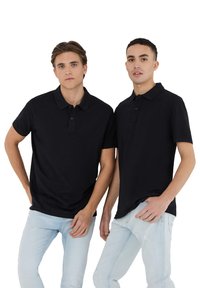 Polo shirt nera a maniche corte con patta abbottonata, indossata con jeans azzurri. Tessuto liscio, vestibilità comoda e design minimalista.