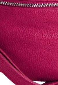 Fuchsia leren handtas met een gestructureerd oppervlak, zilverkleurige ritssluitingen en een gebogen ontwerp met een verstelbare riem.