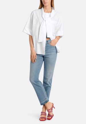Weiße kurze Bluse mit einem großen Schleifenkragen, kombiniert mit hellblauen geraden Jeans und pinken Riemchenabsätzen.