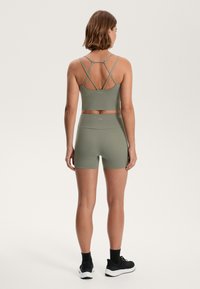 Olíva zöld sport crop top keresztpántos hátrésszel és hozzá illő magas derekú sorttal. Simább, elasztikus anyag. Fekete sportcipők.