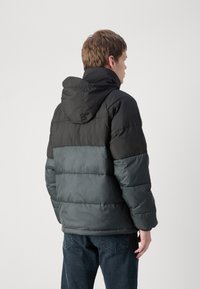 Giacca a vento imbottita con un design a blocchi di colore nero e grigio scuro, dotata di cappuccio e texture trapuntata, realizzata in materiale sintetico.