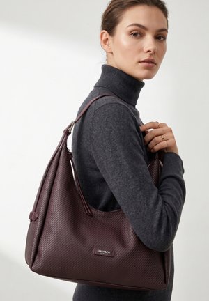 Femme en col roulé gris foncé portant un grand sac à épaule texturé marron foncé avec une étiquette "DIANA&CO FIRENZE".