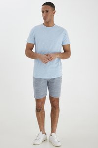 Camiseta azul claro de tejido suave, combinada con pantalones cortos grises texturizados. Zapatillas blancas completan el atuendo casual. No hay patrones ni gráficos visibles.