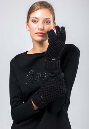 Guanti neri in maglia caratterizzati da un motivo testurizzato e da un polsino a costine, con un piccolo accento metallico vicino al polso, indossati da una persona.