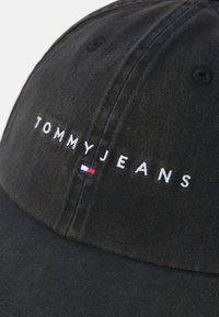 Căciulă din denim negru cu boruri curbate, având broderie albă "TOMMY JEANS" și un accent mic cu logo roșu, alb și albastru pe lateral.