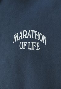 Námornícky modrý sveter s nápisom "MARATÓN ŽIVOTA" v bielej farbe, zakriveným písmom. Materiál vyzerá jemne s hladkým povrchom.