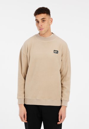 Sweat-shirt en polaire beige avec un col ras du cou, des poignets et un ourlet côtelés, arborant un petit logo de marque noir et blanc sur la poitrine.