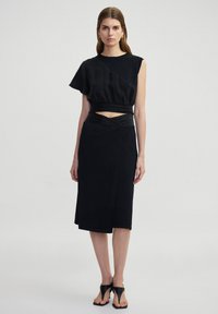 Zwart tweedelig outfit met een asymmetrische top met een uitsnijding bij de taille en een rok tot de knie. Gladde textuur en aansluitend ontwerp.