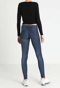 Top negro de manga larga con textura acanalada y dobladillo con puntilla, combinado con jeans ajustados de color azul oscuro. Zapatillas blancas completan el atuendo.