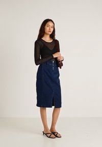 Juodas permatomas ilgarankovė palaidinė dera su iki kelių ilgio tamsiai džiuto sijonu su priekiu iškirpte ir užtrauktuku, papildyta juodais sandalais.