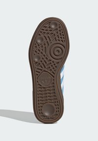 Rjavi gumijasti podplat superge z zapletenimi vzorci in krogi; ima logo in teksturirano podlago za boljši oprijem. Modra zgornjost z belimi črtami.