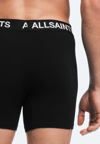 Svarta boxertrosor med en vit logoband i midjan. Tyget verkar slätt med en åtsittande design som framhäver en sömlös konstruktion.