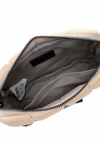 Interno di una borsa a mano in tessuto beige con rivestimento grigio, caratterizzato da più scomparti e una cerniera prominente con denti neri.