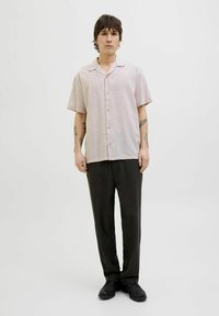 Chemise à manches courtes, rose clair, en tissu texturé, assortie à un pantalon sombre et des chaussures noires. Col simple et coupe naturelle.