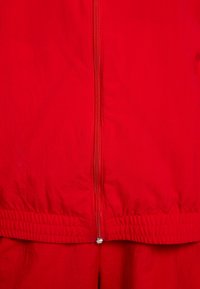 Röd jacka med slät yta, försedd med dragkedja framtill och elastisk midjeband. Enkel design utan extra mönster eller detaljer.