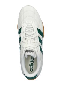 Zapatilla Adidas blanca con rayas verdes, con parte superior de cuero acolchado, cierre de cordones y suela de goma color caramelo. Logo en la lengüeta.