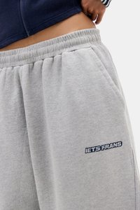Lichtgrijze sweatpants met elastische tailleband, voorzien van zijzakken en geborduurde "IETS FRANS" tekst in marineblauw. Zacht katoenmateriaal.