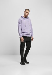 Sudadera morada con cordones y bolsillo frontal, combinada con joggers negros ajustados y zapatillas negras. Tela suave y diseño casual.