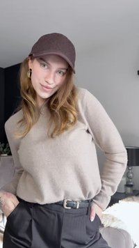 Pull beige en tricot à manches longues, pantalon noir, et casquette marron avec un motif subtil. Ceinture noire avec boucle argentée.