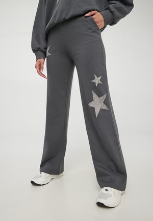 Pantaloni grigi in felpa con motivi a stelle argentate sui lati, realizzati in un materiale morbido, dotati di un design a gamba larga e tasche laterali.