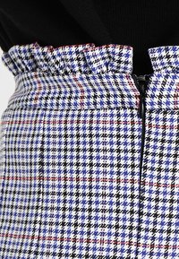 Kostkovaná sukně s modro-černobílým vzorem, s volánkovým pasem a centrálním zipem, vyrobená z texturované tkaniny.