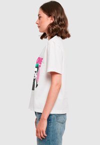 Weißes T-Shirt mit kurzen Ärmeln, das einen auffälligen grafischen Druck einer Figur mit grünen Haaren und Sonnenbrille zeigt, akzentuiert mit rosa und schwarzen Details.