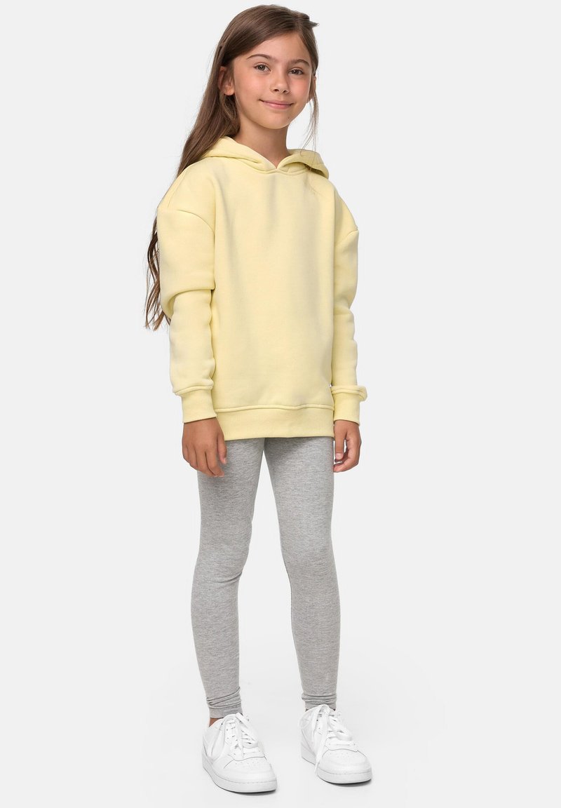 Felpa gialla con vestibilità comoda, maniche lunghe e tasca a marsupio, abbinata a leggings grigi e sneakers bianchi. Design semplice e confortevole.