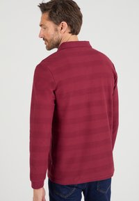 Bordeaux lange mouwen polo met gestructureerde strepen, kraag en zijslitsen. Gemaakt van een zachte stof; heeft een klein logo op de mouw.