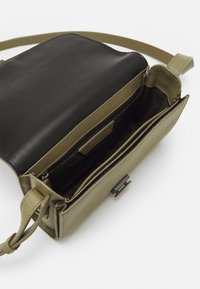 Borsa a tracolla verde oliva con pattina in pelle nera, divisori interni, tasca con zip e texture intrecciata. Includa una tracolla regolabile.