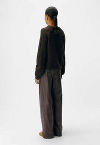 Brauner Strickpullover mit strukturierten Details, kombiniert mit lockeren grauen Hosen. Das Outfit zeichnet sich durch einen lässigen Schnitt und lange Ärmel aus.