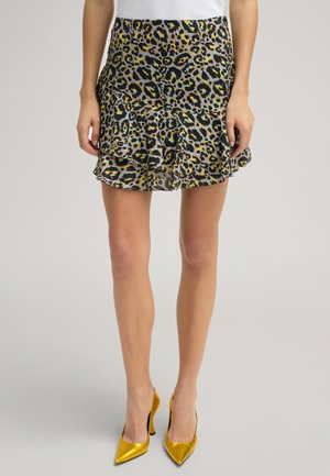 Gonna a volant con stampa leopardata e sovrapposizione trasparente nei toni del giallo, nero e beige. Abbinata a décolleté metallici gialli a punta.