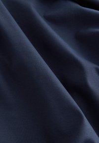 Tissu bleu marine avec une texture lisse et douce, présentant un léger éclat et un drapé subtil, montrant de légers plis ou faux plis.