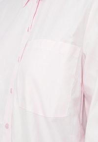 Camisa de botão em rosa claro com um bolso no lado esquerdo do peito, mostrada em close-up.