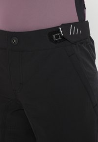 Musta ulkoiluhousut, joissa on teksturoitu kangas, säädettävä vyötärö nappi- ja tarrakiinnityksellä sekä sivutaskut.