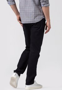 Vaqueros de mezclilla azul oscuro con un corte ajustado, diseño de cinco bolsillos y detalles de costura sutiles. Combinados con zapatillas blancas.