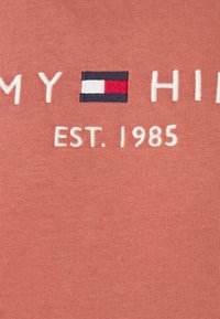 Embroidered red, white, and blue flag with white text "MY HIL" and "EST. 1985" on pinkish fabric background.