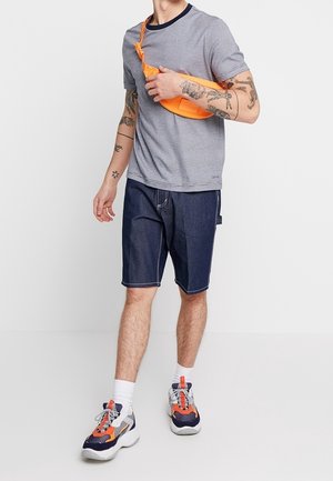 Camisa de manga corta texturizada gris, pantalones cortos de mezclilla azul marino, riñonera naranja y zapatillas deportivas multicolor sobre un fondo claro.