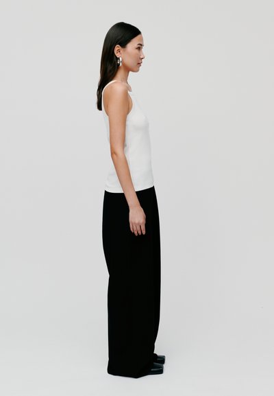 Un maiou alb cu bretele subțiri, asociat cu pantaloni negri largi. Ținuta are un design minimalist și o textură fină.