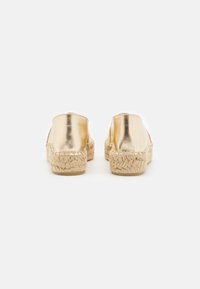 Espadrilles métalliques dorées avec une semelle en jute tissée. Arrière arrondi et design à enfiler. Texture lisse avec un éclat subtil.